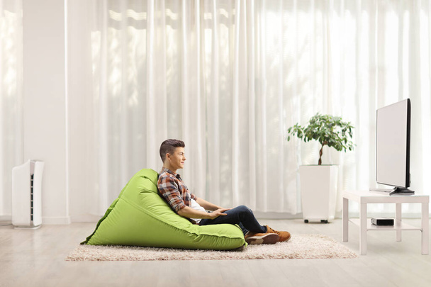 Profile shot of a guy sitting on a green bean bag chair and watching tv - Fotó, kép