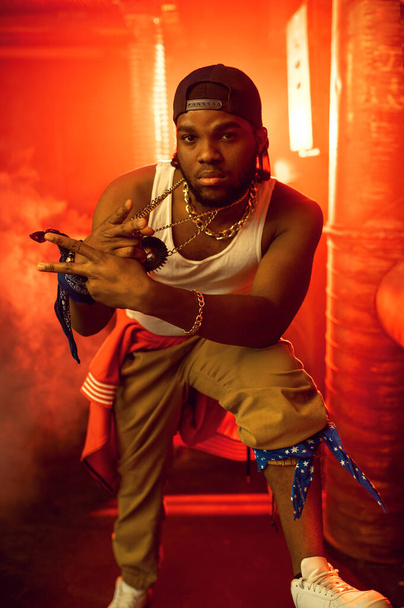 Stijlvolle rapper toont zijn gouden sieraden in studio met koele ondergrondse decoratie. Hip-hop artiest, breakdance - Foto, afbeelding