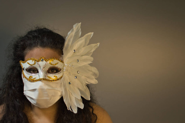 Tmavovlasá žena s karnevalovou maskou a chirurgickou maskou na šedém pozadí, v popředí. - Fotografie, Obrázek