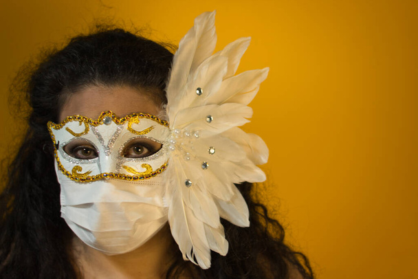 Dark-haired woman with carnival mask on yellow background, in the foreground. - Photo, Image