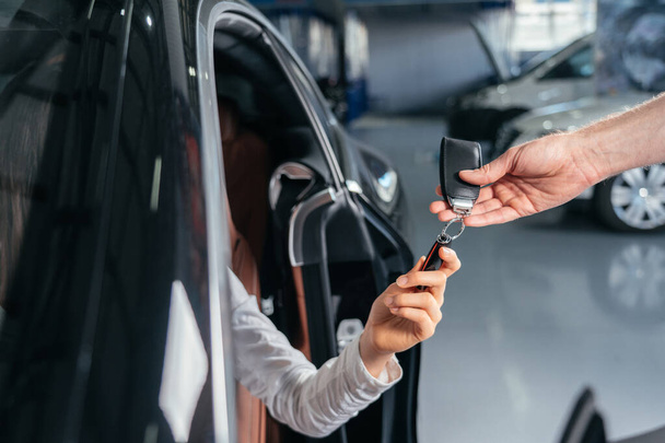 Car dealer is giving key for a new car to young woman - Foto, Imagem
