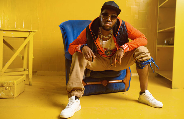Rapper poseren in stoel in studio met gele tinten - Foto, afbeelding