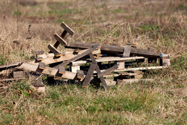 Stos złamanych starych zniszczonych palet drewnianych pozostawionych w lokalnym rodzinnym podwórku otoczony częściowo suchą trawą w zimny słoneczny zimowy dzień - Zdjęcie, obraz