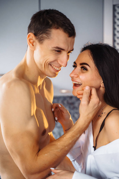 Close-up of a laughing couple in love. Guy and girl hugging tenderly in the kitchen. Foreplay before hot sex, at night. Joking, smiling at each other in the soft, warm yellow light. - Photo, Image