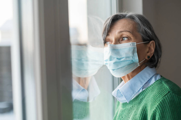Senior lady in a face mask looking at the window - Photo, image