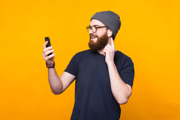 Photo of bearded hipster man looking at smartphone and listening music at earpods - Foto, afbeelding