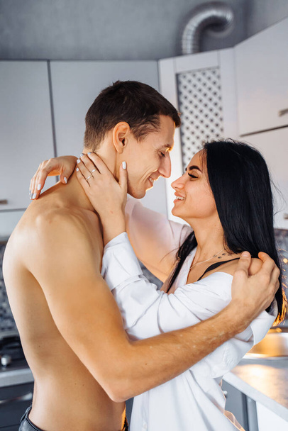 Lähikuva nauravasta rakastuneesta parista. Mies ja tyttö halaavat hellästi keittiössä. Esileikkiä ennen kuumaa seksiä öisin. Pilailemme, hymyilemme toisillemme pehmeässä, lämpimässä keltaisessa valossa. - Valokuva, kuva