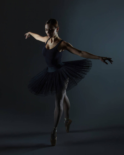 attractive ballerina poses gracefully in the studio on a black background - Photo, image