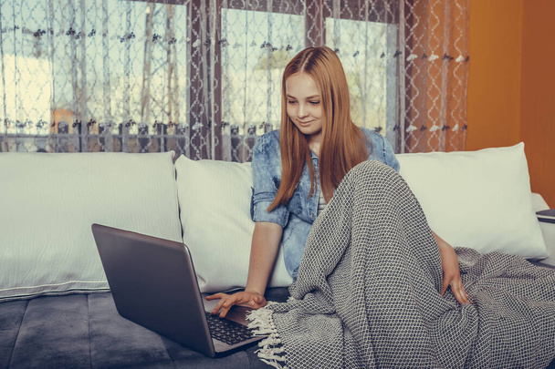 Девочка-подросток смотрит видео в Интернете веб-бинар, обучаясь на ноутбуке сидя, накрытый одеялом в постели. Курс для студенток, видеоконференция или видеозвонок дома. - Фото, изображение