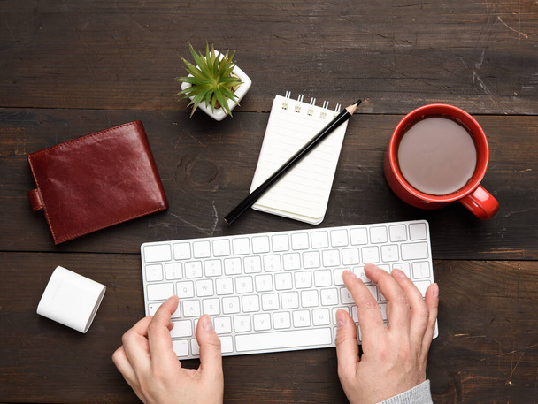 Kablosuz klavye ve iki el, kahve, işyeri, üst görünümü olan bir bardağın yanında, ahşap bir masaya yazı yazıyorlar. - Fotoğraf, Görsel
