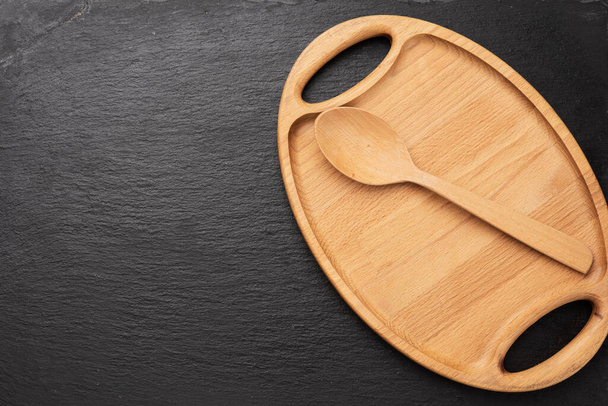 wooden spoon and empty oval brown wooden tray board on a black background, top view - Photo, Image