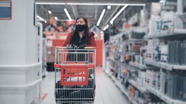 La donna che indossa una maschera e guanti guida un carrello in un negozio - Filmati, video