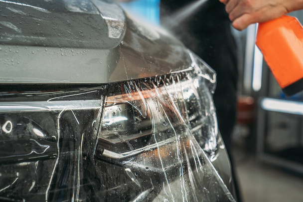 Process of installing of Paint Protection Film or PPF on new car in professional auto Detailing Center. Thin polyurethane film or polymer as protective skin from scratches and rock chips - 写真・画像
