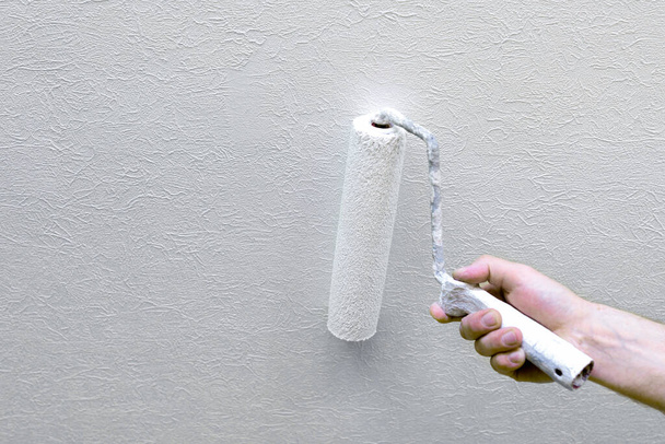 Tamirat sırasında boyayla duvar boyar ve boya silindiri kullanır. Duvar kağıdıyla kaplı bir duvarı boyama işlemi. Boşluğu kopyala - Fotoğraf, Görsel