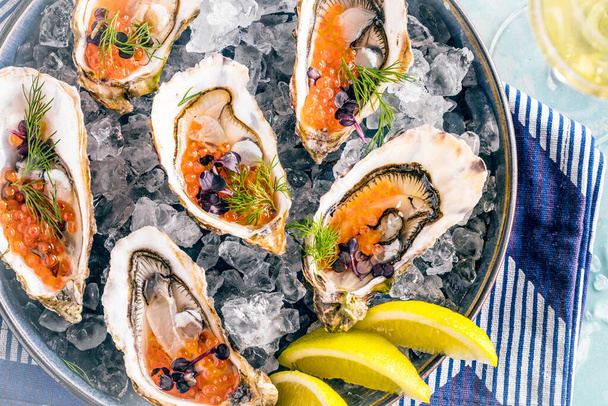 close-up view of delicious oysters platter with lemon, caviar and ice served on blue table. - Foto, Imagem