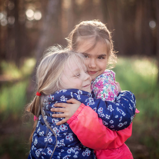 Linda chica abrazando a su hermana pequeña con amor y ternura durante su caminar en el bosque en otoño, abrazo nacional y día de la amistad, estilo de vida casual, al aire libre - Foto, imagen