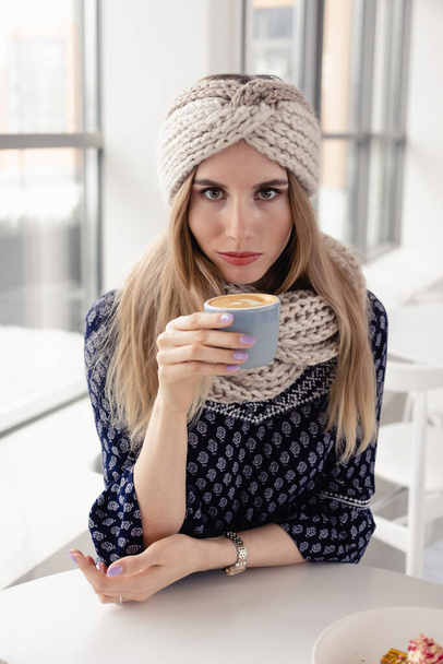 Beautiful cute winter girl wearing knitted hat and mittens with coffee mug. Attractive girl with hot drink on cafe background.  Drinking coffee and enjoying life. - Foto, afbeelding