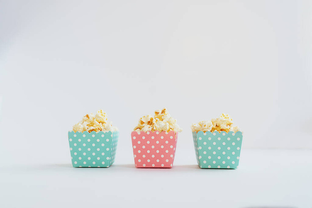 A row of blue and pink decorative small patterned paper boxes with popcorn on the white background. Child portion. Copy space, selective focus. - Fotó, kép