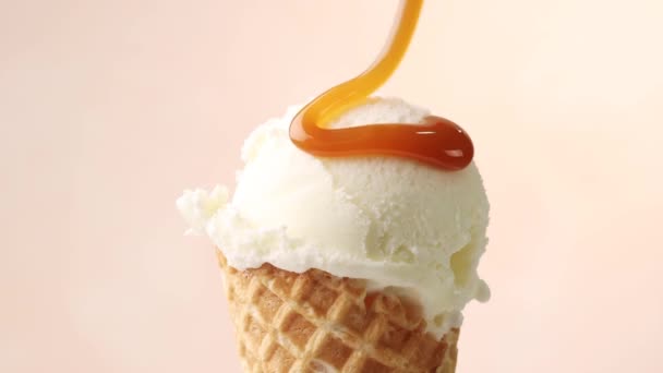 melted caramel sauce flowing on vanilla ice cream scoop in waffle cone close up on beige background. perfect summer dessert - Footage, Video
