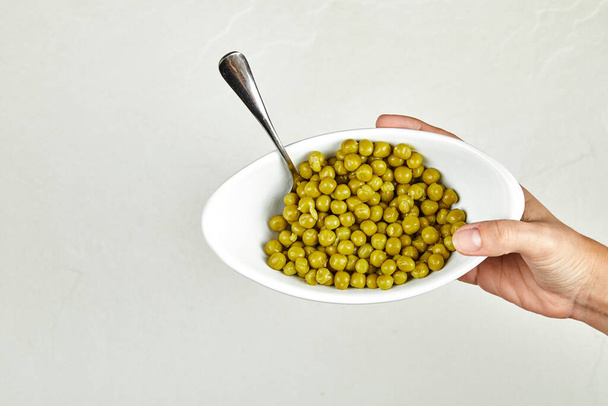 Hand hält eine Schüssel gekochter grüner Erbsen auf weißem Hintergrund - Foto, Bild