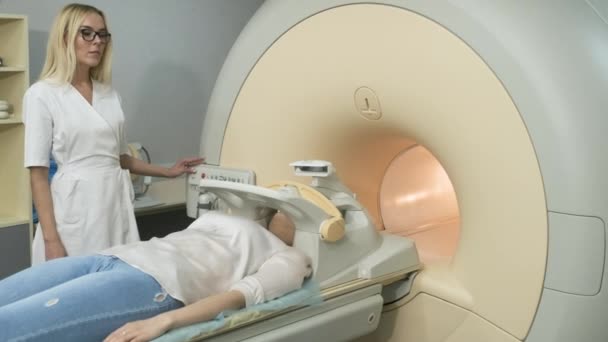 Radiolog robi tomografię mózgu, głowy, szyi. Młoda pacjentka na automatycznym stole wchodzi do maszyny rezonansowej typu zamkniętego przy użyciu nowoczesnego sprzętu, cewki na głowie pacjenta. - Materiał filmowy, wideo