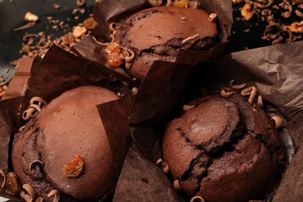 チョコレートのフォンダンケーキ、クルミのチョコレートマフィン、レーズンとすりおろしたチョコレート、ダークブラックの背景にダークチョコレートバー。レシピ本の作成に最適. - 写真・画像