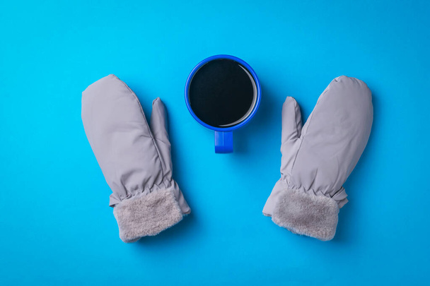 Manoplas cálidas para mujer y una taza de café sobre un fondo azul. Bebida caliente y mitones. - Foto, Imagen