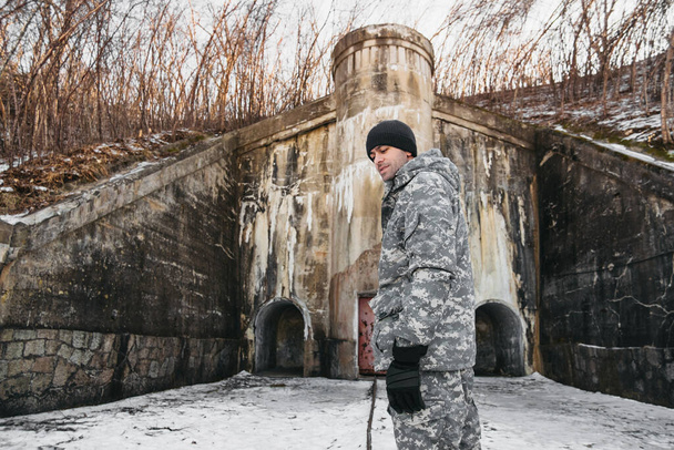 homem em roupas de camuflagem militar no fundo da paisagem de inverno perto de um castelo de concreto velho. turismo local interessante, foco seletivo - Foto, Imagem