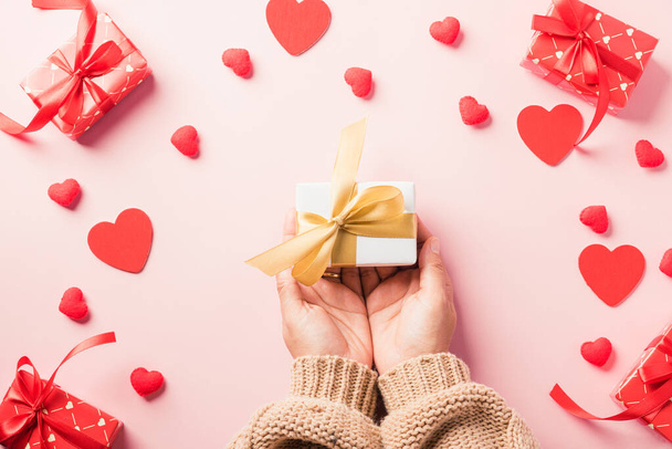 Valentine's day and birthday. Woman hands holding gift or present box decorated and red heart surprise on pink background, Female's hand hold gift box package in craft paper Top view flat lay - Φωτογραφία, εικόνα