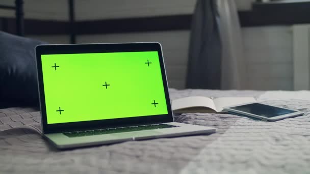 Un portátil abierto se encuentra en la cama en el interior de una casa. Pantalla verde con marcadores de seguimiento. El portátil, el portátil y la tableta que se encuentran en la colcha. - Metraje, vídeo