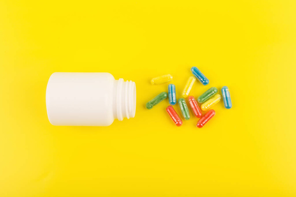 Flat lay with white medication bottle with spilled multicolored pills against yellow background - Фото, зображення