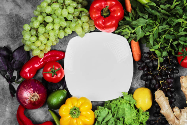Hrozny, paprika, zelenina, citron, rajče, zázvor a bílý talíř na mramorovém pozadí - Fotografie, Obrázek