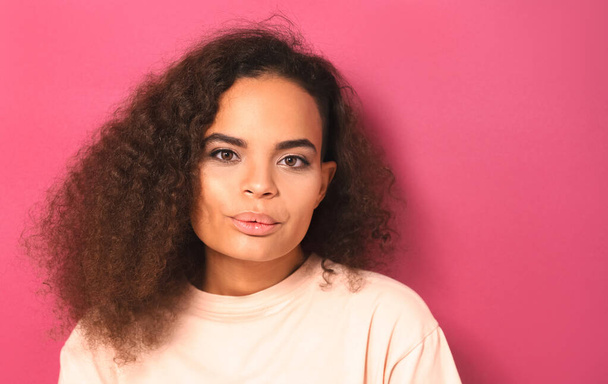 Whistling lips folded happy beautiful young African American woman looking positively at camera wearing peachy t-shirt isolated on pink background. Beauty concept - Photo, image