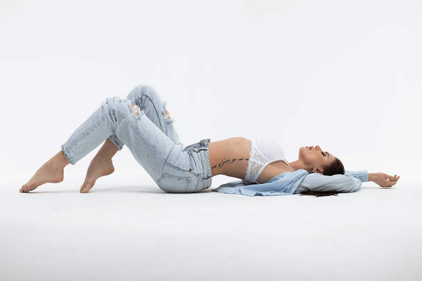 Mladý svůdný ženský model v podprsence a košili s džínovým oblečením stojící se zvednutými pažemi při pohledu na kameru - Fotografie, Obrázek