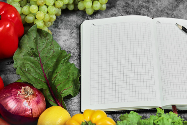 Hrozny, paprika, zelenina, citron, rajčata a prázdný notebook na mramorovém pozadí - Fotografie, Obrázek
