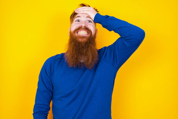 Oops, what did I do? handsome red haired bearded Caucasian man standing against yellow wall  holding hand on forehead with frightened and regret expression. - Photo, Image