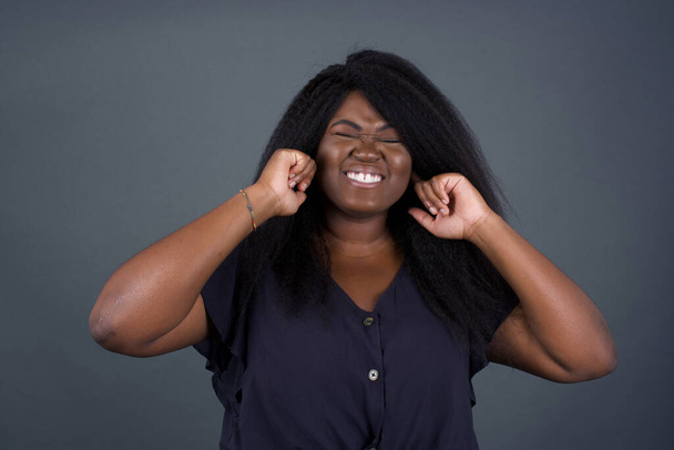 Stop making this annoying sound! Headshot of unhappy stressed out young African American woman posing over grey background making wry face, plugging ears with fingers, irritated with loud noise coming from neighbours who live above her. - Zdjęcie, obraz