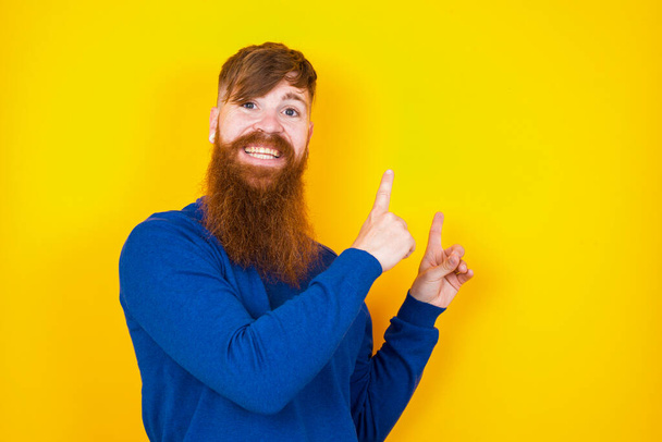 ポジティブなハンサムな赤毛のひげを被った白人男性は,2本の指で笑顔を浮かべ,空のコピースペースを見ています. 広告コンセプト. - 写真・画像