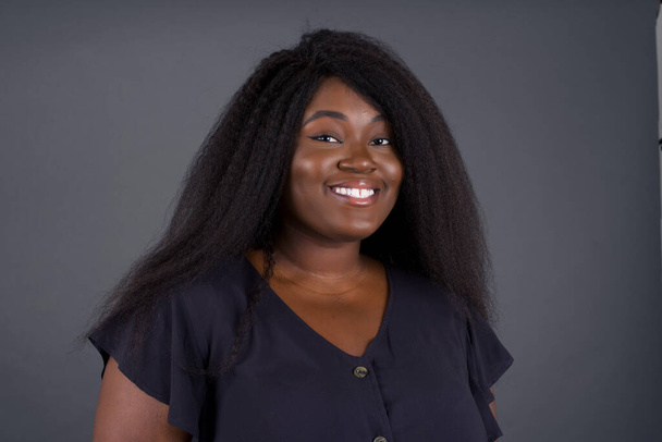 красивая афроамериканка позирует на сером фоне улыбаясь  - Фото, изображение