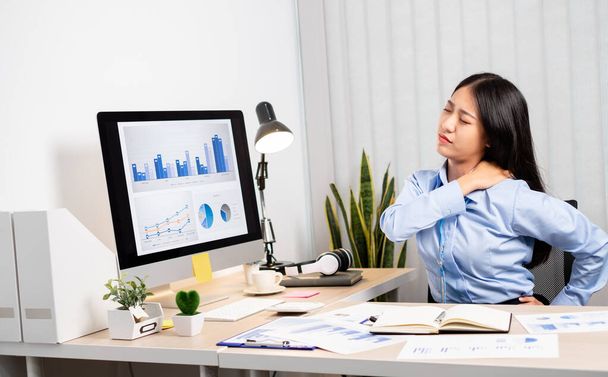 Aziatische vrouwelijke accountant is moe van het werken in een stoel, rekken om te ontspannen en te ontspannen tijdens het werken hard op kantoor. - Foto, afbeelding