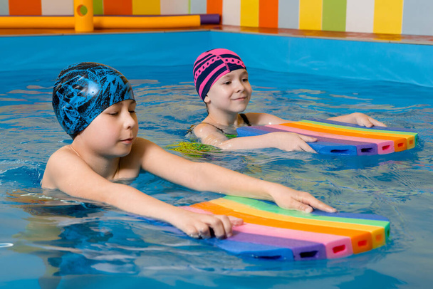 Boy and girl wearing swimsuit uses a foam pad to practice swimming in swimming pool - Photo, Image