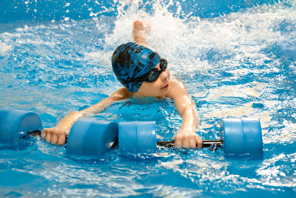 Хлопчик плаває з водяними гантелями в руках у басейні
 - Фото, зображення