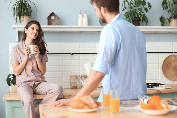 Piękna młoda para w piżamie patrzy na siebie i uśmiecha się podczas gotowania w kuchni w domu - Zdjęcie, obraz