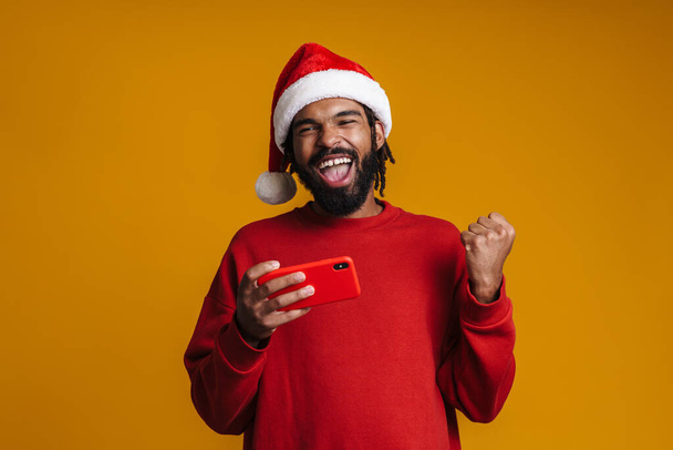 Excited african american guy making winner gesture while using cellphone isolated over yellow background - Fotoğraf, Görsel