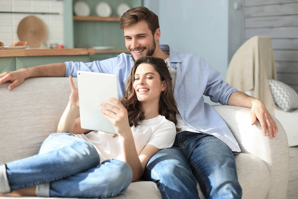 Young couple watching media content online in a tablet sitting on a sofa in the living room - Fotografie, Obrázek