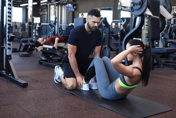 Trainer helping young woman to do abdominal exercises in gym - Zdjęcie, obraz