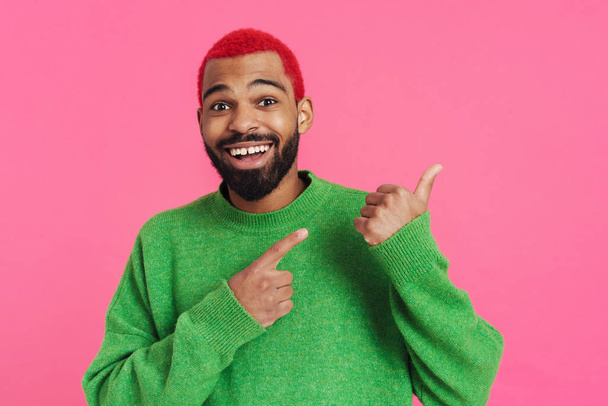 Excited african american guy smiling and pointing fingers aside isolated over pink background - Foto, imagen