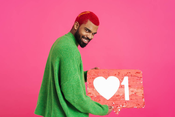 Cheerful african american guy smiling and showing placard isolated over pink background - Foto, Imagen
