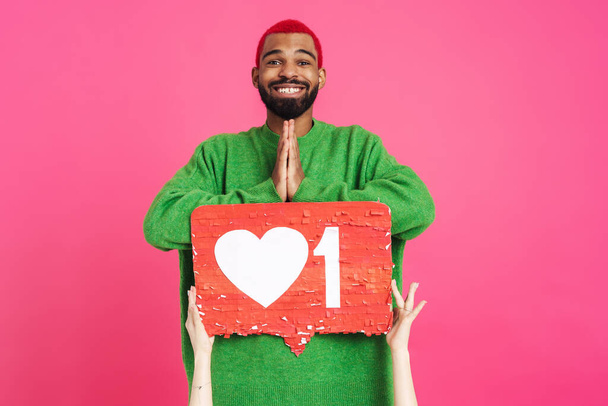 Joyful african american guy holding palms together while posing with placard isolated over pink background - Photo, image