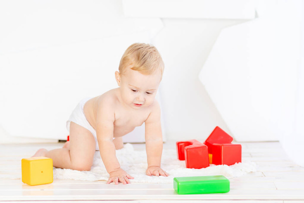 a small child a boy of six months plays with bright cubes in a bright white room in diapers - Photo, Image
